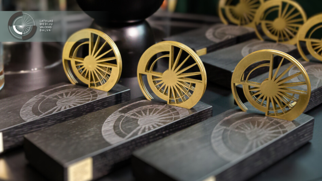 Latvijas Mediju valodas balvas statuetes ar melnu pamatni un zelta aplī veidotu dizainu, kas atgādina stilizētu saules staru simbolu.