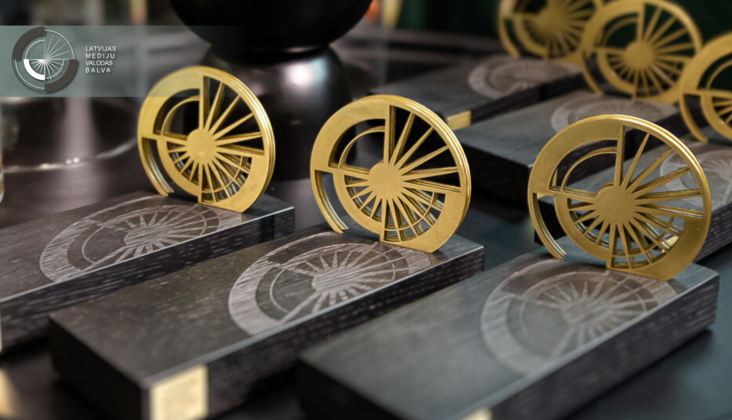 Latvijas Mediju valodas balvas statuetes ar melnu pamatni un zelta aplī veidotu dizainu, kas atgādina stilizētu saules staru simbolu.